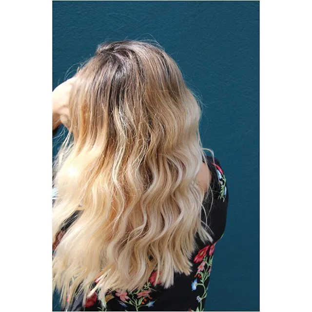 Warm-blonde balayage waves against a teal wall