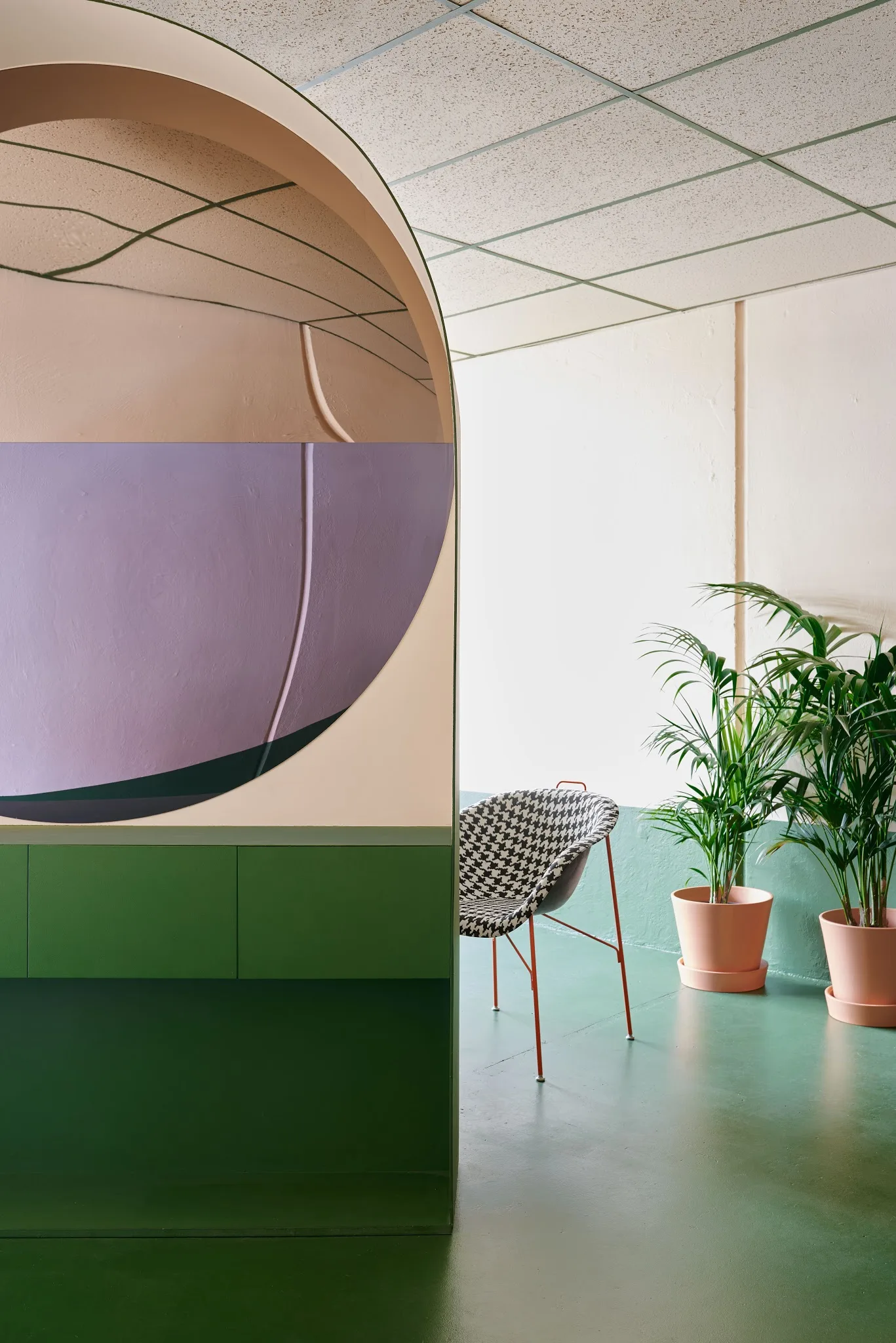 Inside Hues Hair — the rounded peach archway, lilac abstract wall panel, emerald-green cabinetry and floor, two potted palms and the houndstooth tub chair